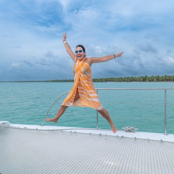 Woman jumping happily on the catamaran deck in front of the ocean