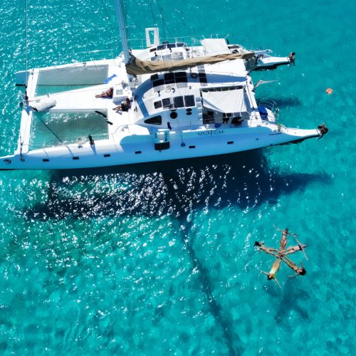 Catamaran vue du ciel amarré, dans une eau cristalline, avec un groupe de femmes formant une étoile dans l'eau