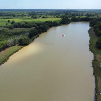 Large grassy field adjacent to the waterskiing area under a clear sky