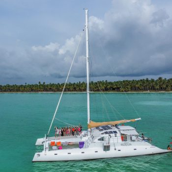 White and red catamaran floating in calm green-blue water near Saona