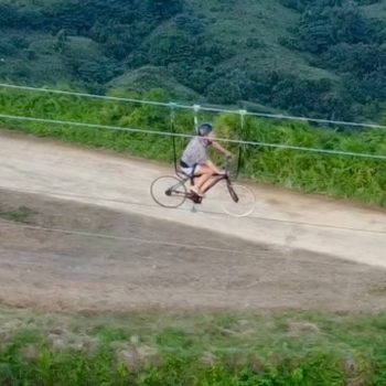 Tourist riding a suspended bicycle in the air with mountains in the background