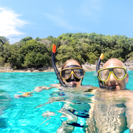 Couple qui se prend en photo dans l'eau turquoise avec equipement de masque et tuba, en arrière plan on aperçoit les falaises de l'ile de catalina